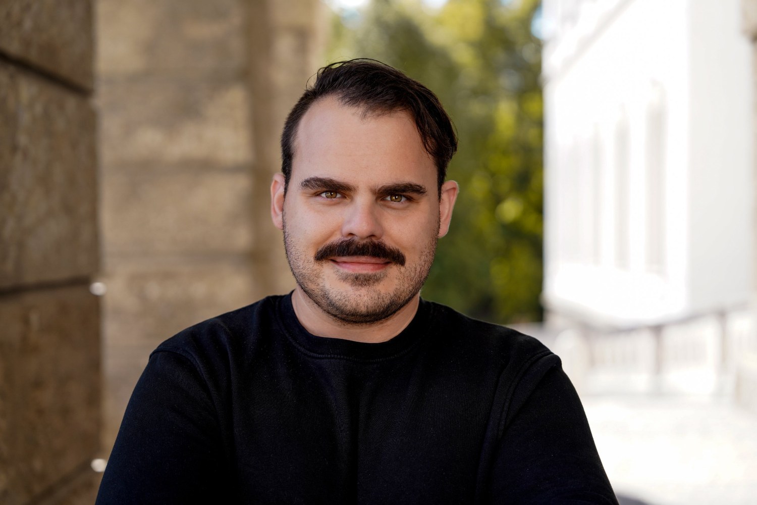 Johannes Egger, founder of HistoryBytes, smiling in a black sweater in front of a historic stone wall in Salzburg